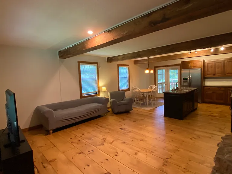Living area with open exposed beams and lots of natural light. House is furnished with living room furniture, tv, dining table.