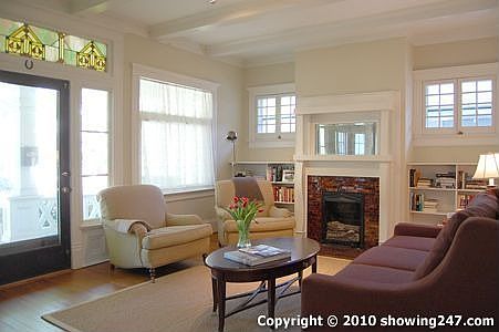 Living room with oversized windows on 2 walls, box beam deiling, halogen track lighting, decorative fireplace (1 of 4) and builtin bookcases.