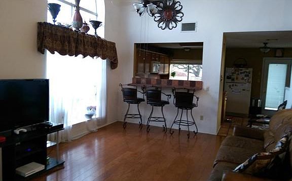 Front family room with wooden floor leading to the open kitchen with three chair bar.