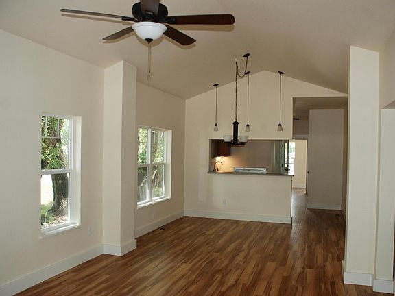 Open design living room, dining room, and kitchen with ceiling fan and vaulted ceilings.