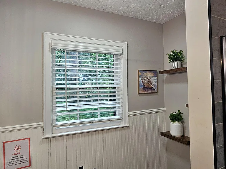 Updated bathroom with tiled walk-in shower, window for natural light, and built-in corner shelving for toiletries.