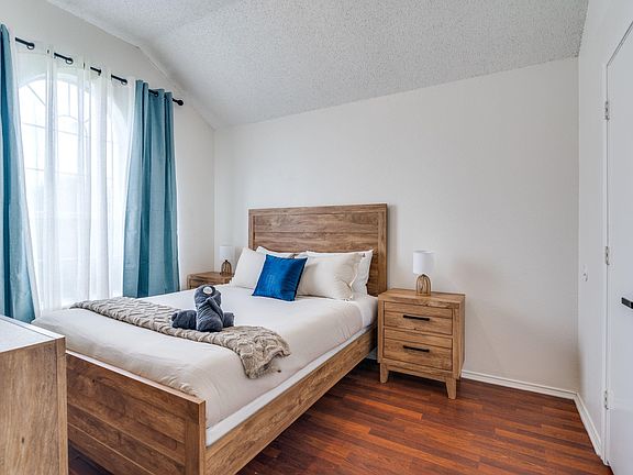 Furnished bedroom with a wood bed frame, matching nightstands, and a large window with curtain panels for natural light.