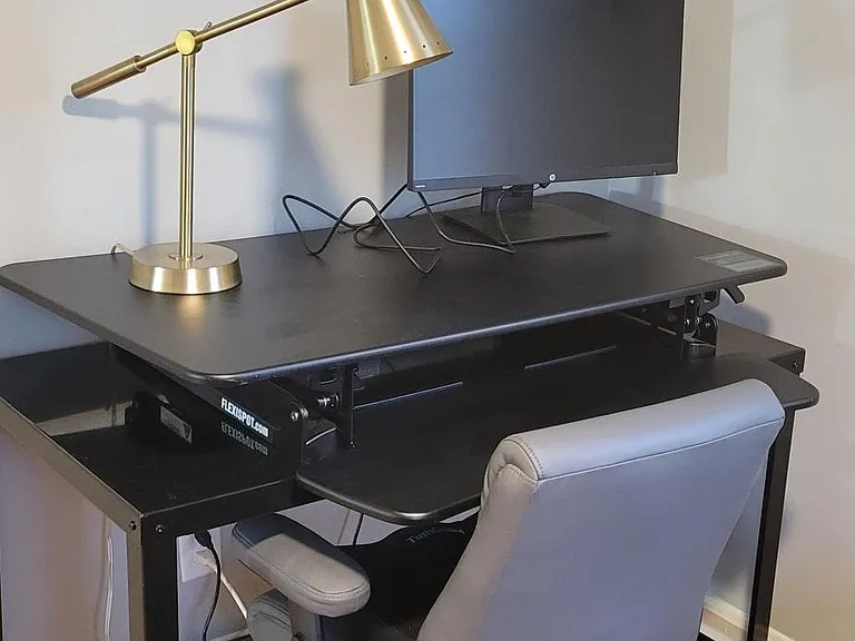 Work station in second bedroom which includes a sit-stand desk, desk chair, and monitor.