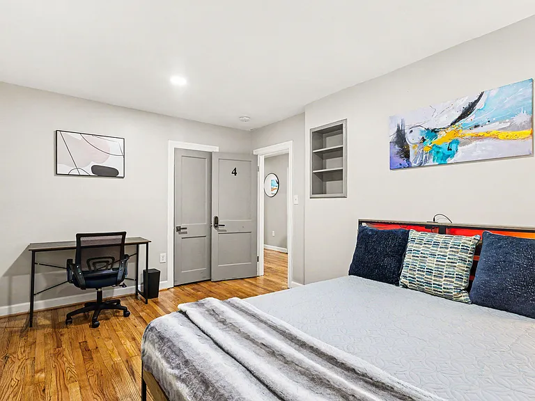 Furnished bedroom with hardwood floors, a work desk, and convenient built-in shelving near the entry.