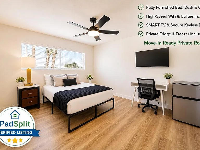 Furnished private bedroom with full bed, work desk and chair, wall-mounted TV, ceiling fan, and in-room mini fridge.