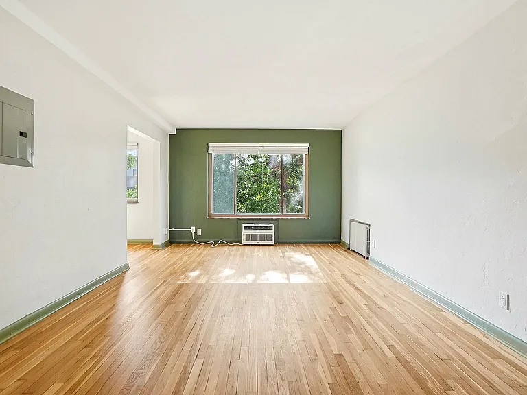 Inviting living room with elegant hardwood floors, a large sunlit window, and a stylish accent wall.