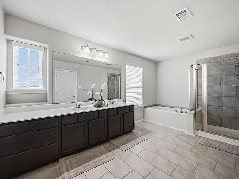 Spacious bath with double-sink vanity, oversized mirror, soaking tub, and a glass-enclosed tile shower.