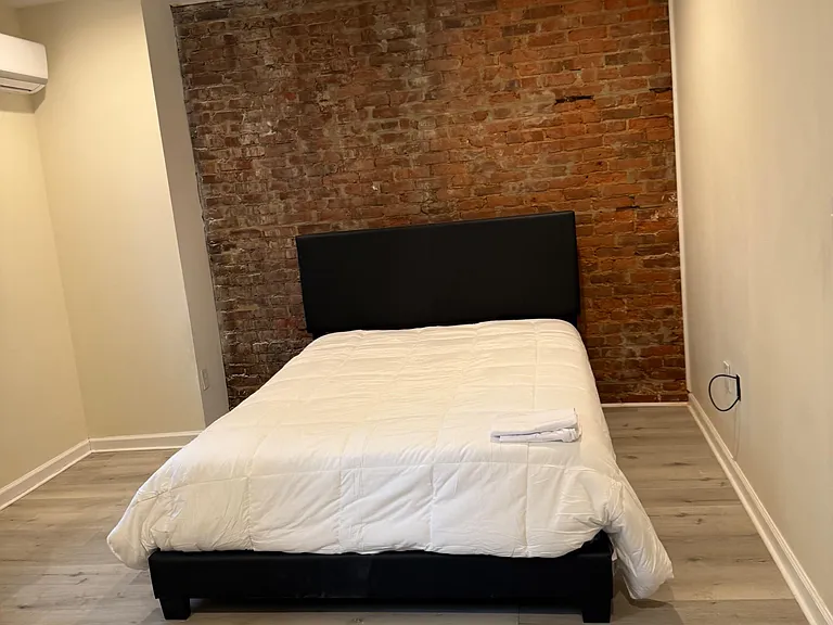 Private bedroom with exposed brick accent wall, recessed lighting, and wood-style floors with mini-split A/C.