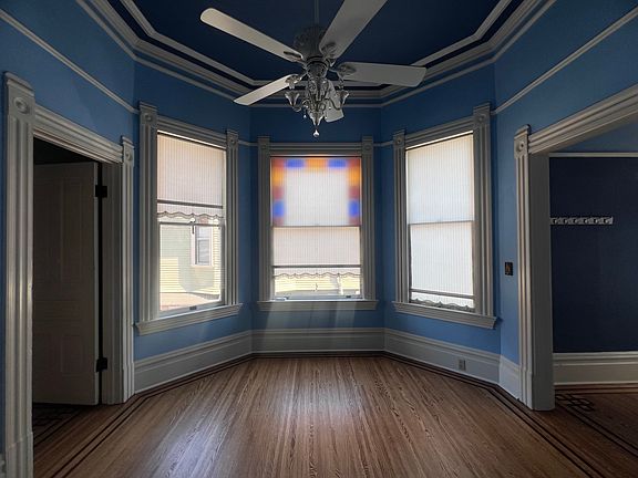 Spacious main living room with bay window, high ceilings, ornate crown moulding and ceiling fan chandelier. Inlaid custom red oak flooring throughout this unit is in excellent condition.