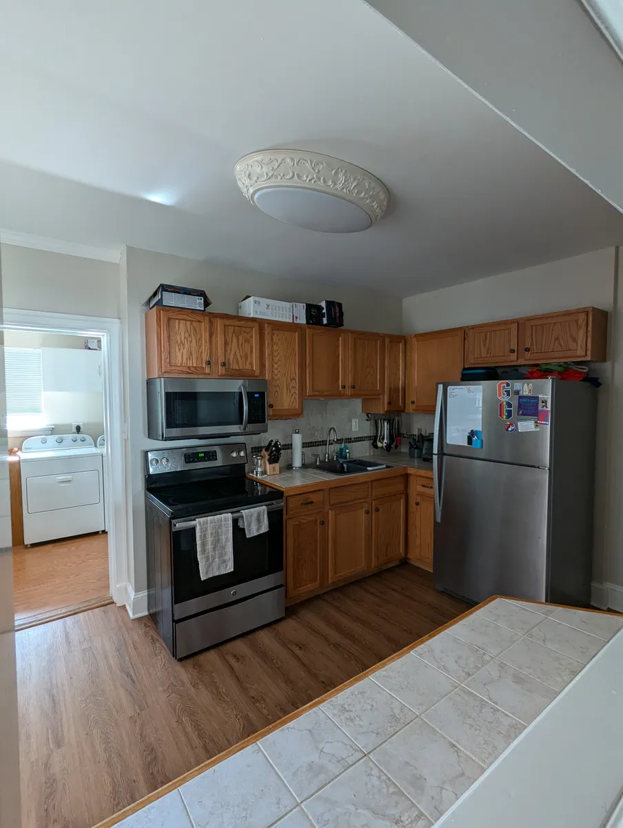 View of kitchen through window from dining room showing fridge, sink, oven, microwave and cabinets (breakfast bar in foreground). - 222 N Darlington St