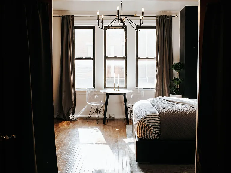 Private bedroom with hardwood floors, three large windows, and space for a bed plus a small table or work nook.