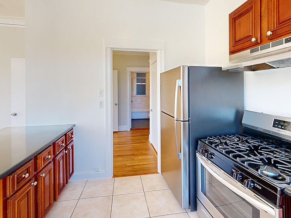 Kitchen with multiple cabinets, refrigerator, stove, range hood, and sink