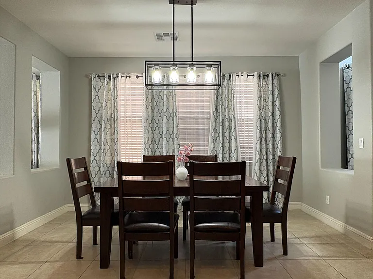 Dedicated dining area with a full-size table, statement pendant lighting, and multiple windows with blinds and curtains.