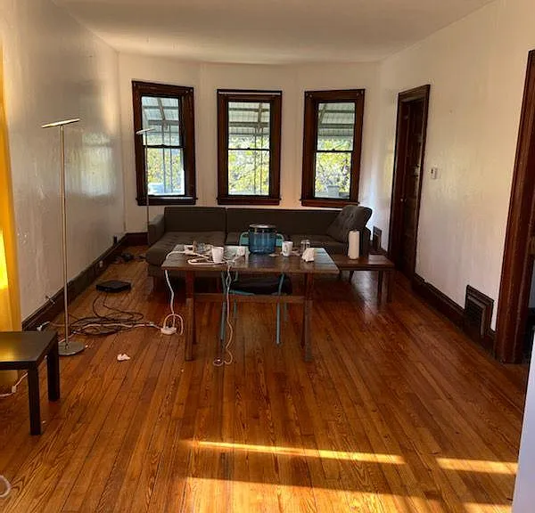large living room with wooden floor, west facing windows towards the private upper porch and the Linden trees, and south facing windows letting in the sunshine