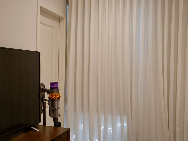 Bedroom 2: Features a functional dresser wall and closed closet door, situated next to window panes styled with included blackout shades and floor length sheer curtain.