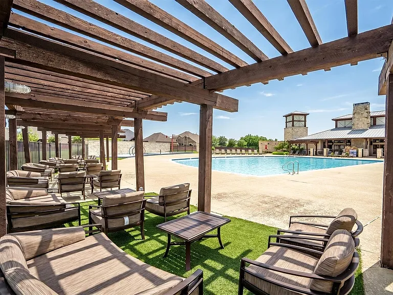 Expansive outdoor pool area featuring a large swimming pool, a substantial clubhouse with stone accents, and an extensive pergola structure