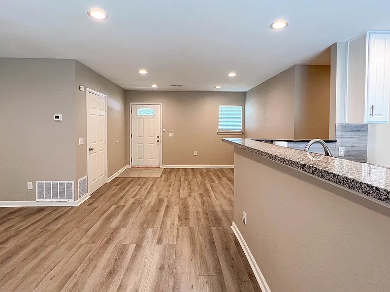 Open living and kitchen area from the opposite view, highlighting the easy flow, wood-look flooring, and granite breakfast bar.