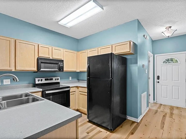 Kitchen area featuring light wood cabinetry, a double basin stainless steel sink, black appliances, and light countertops