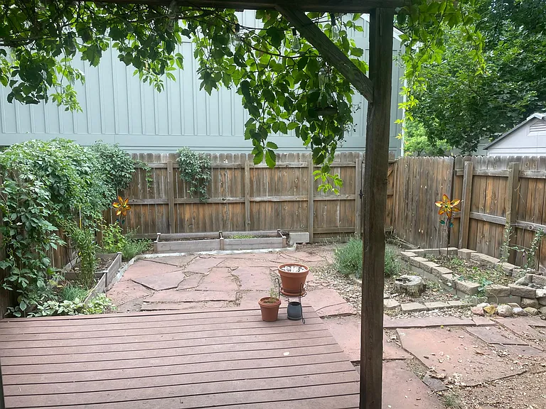 Private fenced backyard with trex deck and pergola and raised garden beds.
