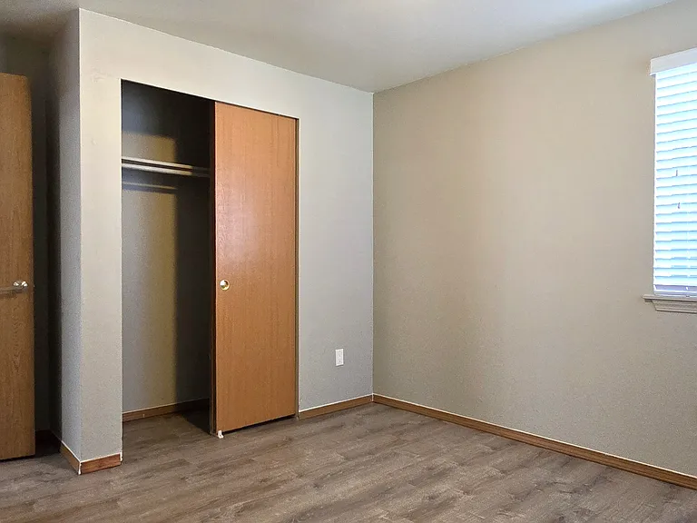Inviting guest bedroom with wood-style flooring, neutral finishes, and a sunlit window. Features a roomy closet and a flexible layout, ideal for guests, a home office, or extra living space.