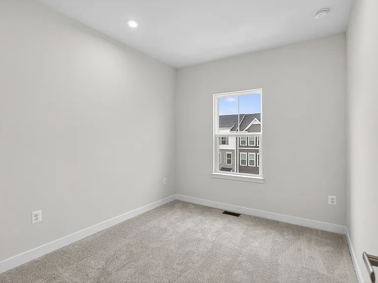 View into bedroom 2; plush carpeting, windows overlooping the front of the house