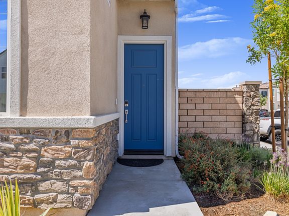 Welcoming front entrance featuring a stylish blue door, stone-accented exterior, and landscaped walkway. Adds charm and curb appeal while providing a warm and inviting first impression to this modern Menifee home.