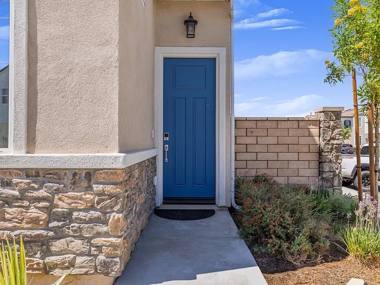 Welcoming front entrance featuring a stylish blue door, stone-accented exterior, and landscaped walkway. Adds charm and curb appeal while providing a warm and inviting first impression to this modern Menifee home.