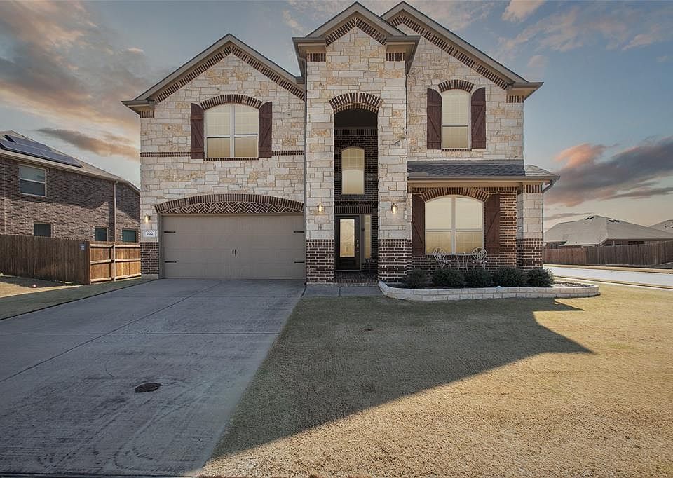 French country style house with an attached garage, brick siding, fence, driveway, and a front lawn