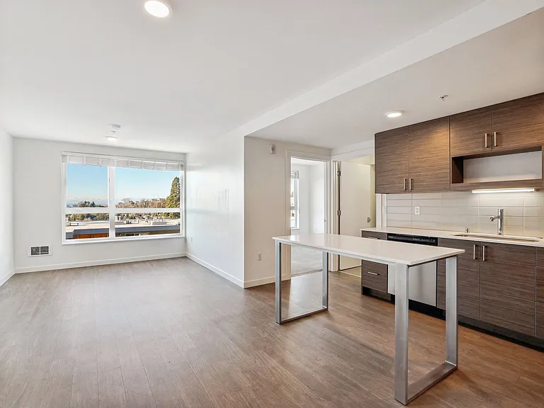 Spacious open-concept living room and contemporary kitchen at 4400 Alaska in Seattle, WA. Features include modern dark cabinets, white island, and large wind...