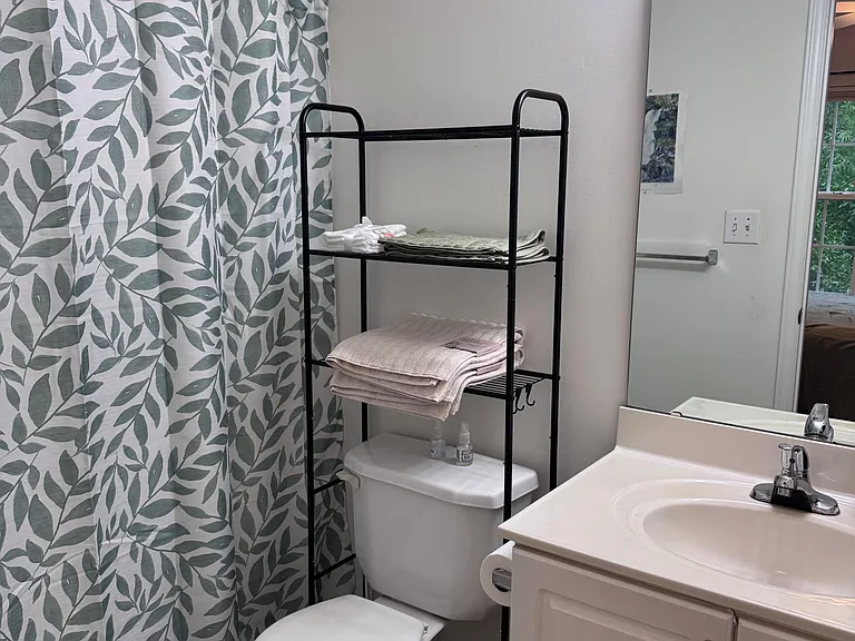 Full bathroom with tub/shower combo, large vanity mirror, and convenient shelving for towels and toiletries.