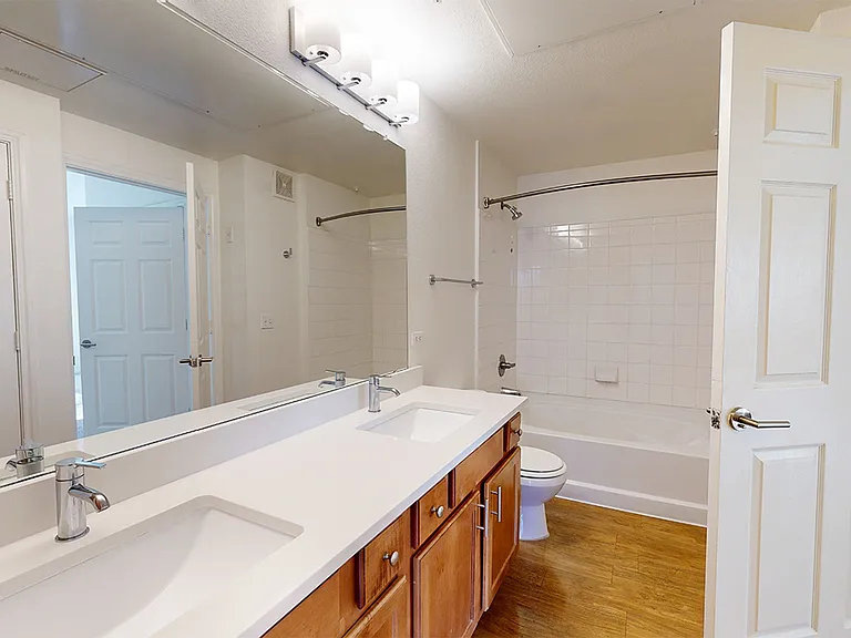 Apartment bathroom with wood-style flooring. Quartz-style countertops (shown here) are available in select homes.