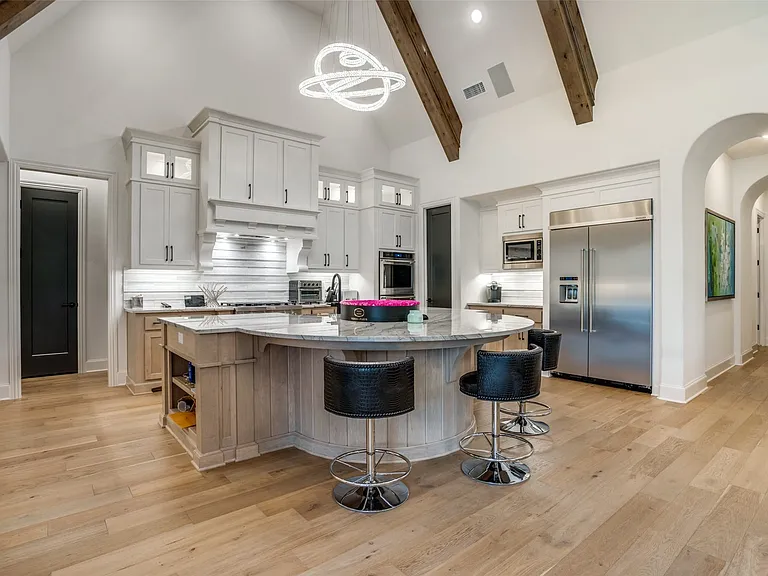 Kitchen featuring a curved central island with seating, a vaulted ceiling with exposed wood beams, and light wood-finish flooring