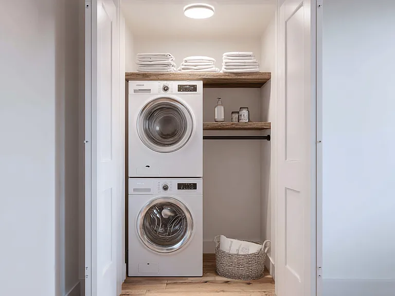 In-unit laundry closet with full size stacked washer and dryer, fixed shelving for storage, and convenient hallway access.