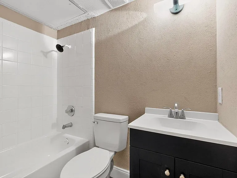 Bathroom with a textured wall, vanity, and shower / bath combination
