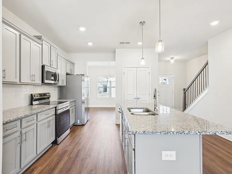 Modern kitchen with white cabinets and granite countertops, flowing seamlessly to the staircase.