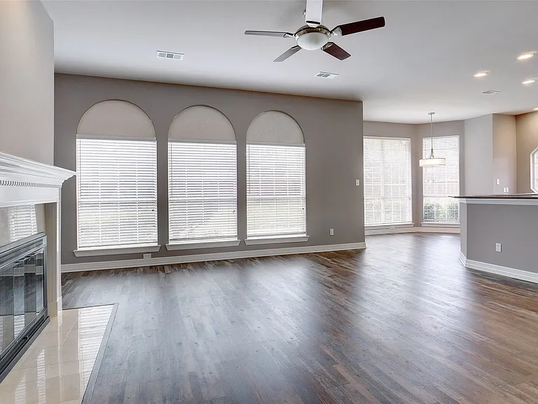 Spacious living area featuring wood-finish flooring, a white mantel fireplace with a tile hearth, and arched windows