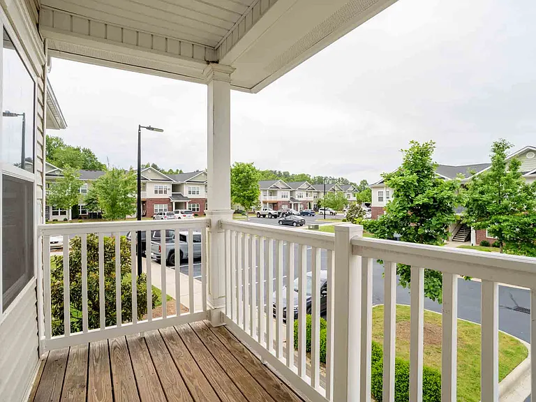 Second-floor private balcony with white railing and scenic views of the Cedar Terrace apartment community and parking area.