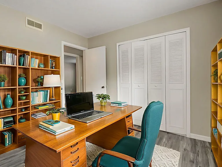 Inviting home office with stylish wooden desk, cozy teal chair, and well-organized bookshelves, perfect for productivity and focus.