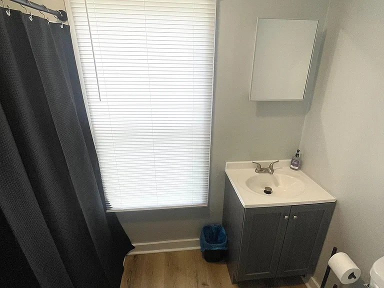 Full bath with a tub/shower combo, vanity with cabinet storage, and a window with blinds for privacy and light.