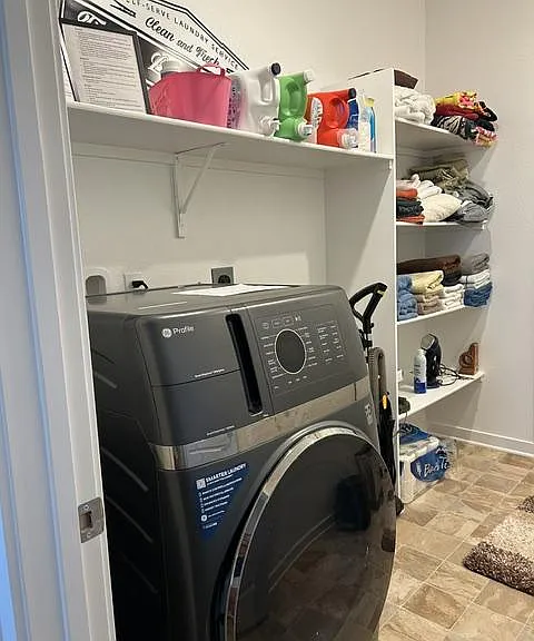Dedicated laundry nook with front-load washer and open shelving for detergents, towels, and household essentials.