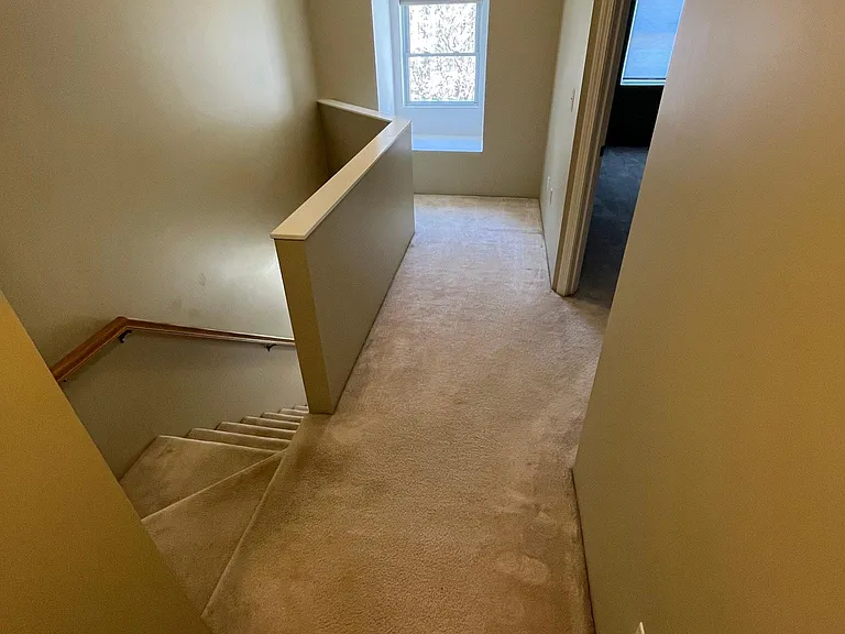 Hallway on upper level stairs lead to lower level front entrance, kitchen, living room, and dining room. View looking toward 2nd bedroom on right.