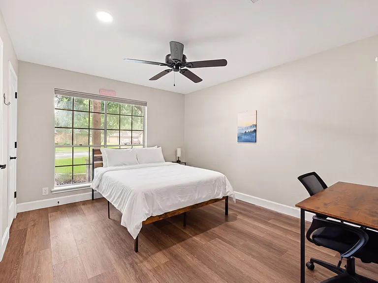 Spacious bedroom with large window, ceiling fan, and desk areaideal for comfortable living and working from home.