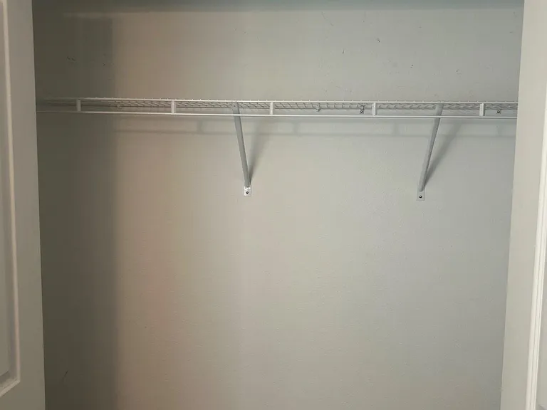 Spacious closet with a full-length shelf and hanging rod, offering practical storage for clothing and daily essentials.