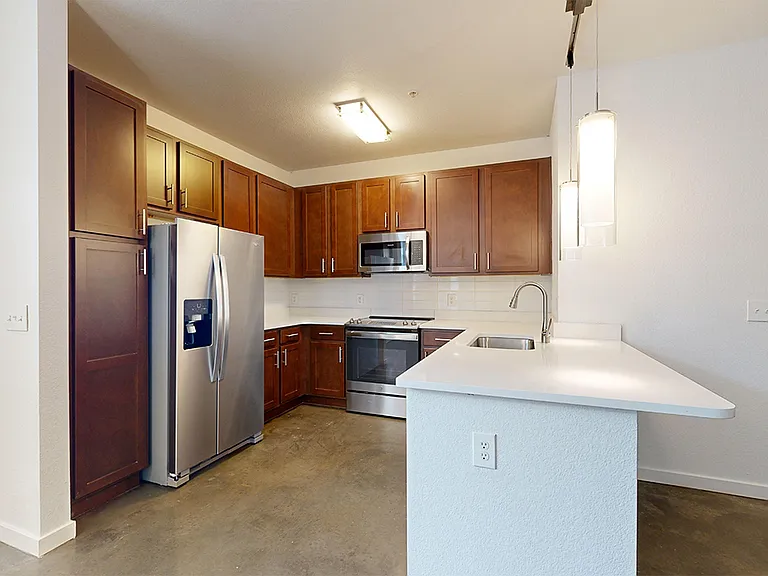 Apartment kitchen with stainless steel appliances, quartz countertops and polished concrete flooring.