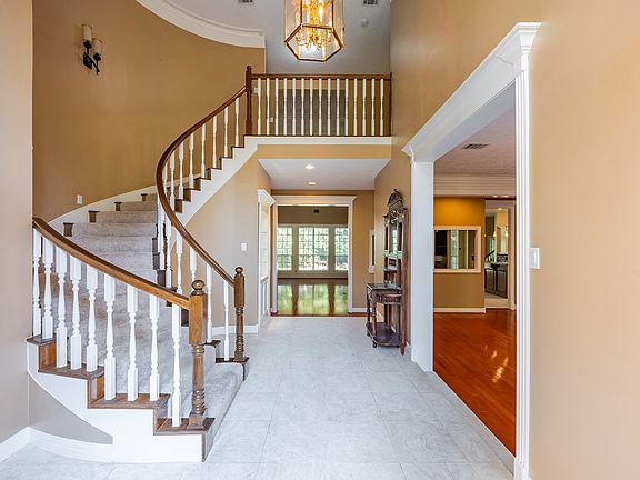 Impressive grand entrance featuring soaring ceilings and a sweeping curved staircase, accented by an open balcony and elegant lighting fixtures that create a striking first impression.