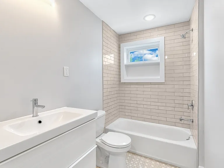 Full bathroom has tiled tub/shower, floating vanity, and stacked washer/dryer.