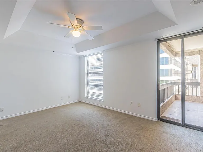 Spacious room featuring tray ceiling, ceiling fan, carpet flooring, a large window with blinds, and sliding glass doors opening to a private balcony