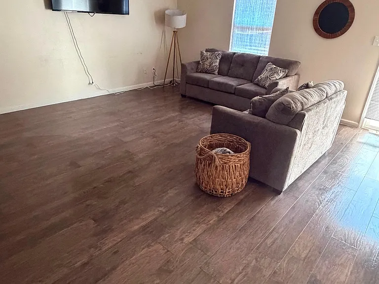 Spacious living area with wood-style flooring, comfortable seating, and a mounted TVideal for relaxing or movie nights.