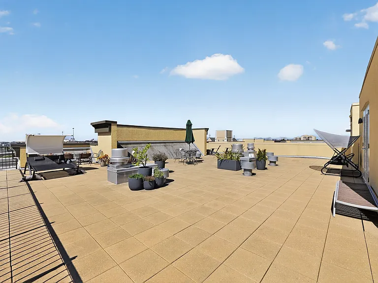 Spacious rooftop terrace with lounge seating, planters, and open sky views.