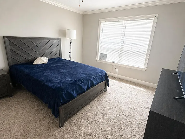 Spacious bedroom with a large window, plush carpet, ceiling fan, and room for a full/queen bed and TV setup.